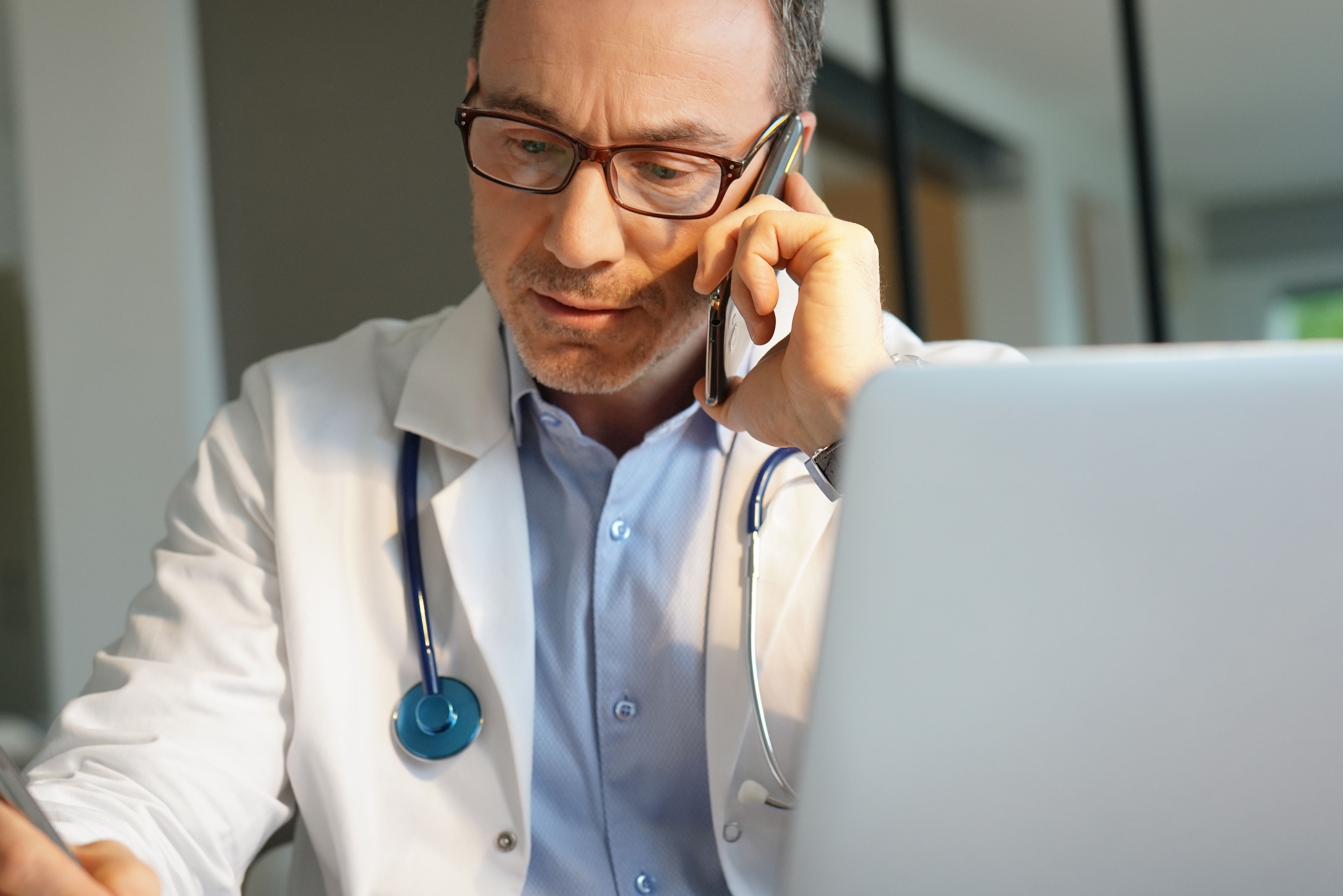 Physician reviewing a patient's history on a laptop while on the phone